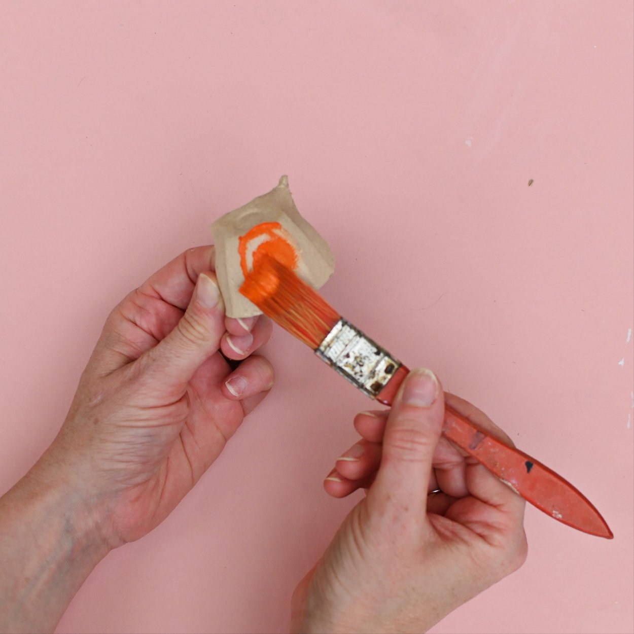 Image shows someone painting the cut out egg carton with orange paint.